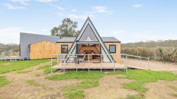 Una casa moderna con techo triangular, una terraza de madera y un área exterior cercada.
