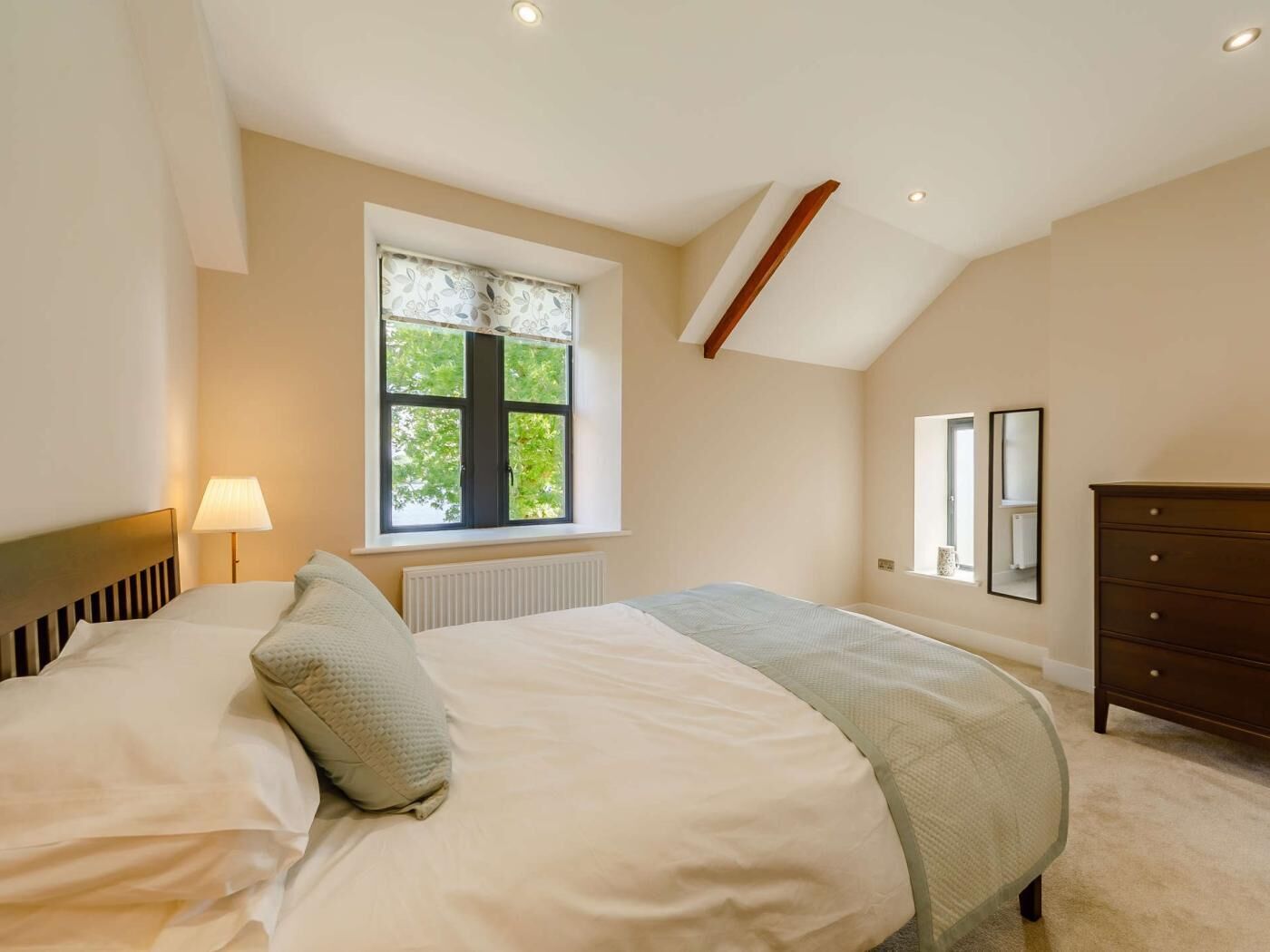 A bedroom with a bed, a window, a dresser, and a radiator.