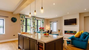 A modern kitchen with a central island, pendant lights, and a dining area with a blue sofa. - 2 Bed in Brampton (oc-88663) (Brampton)