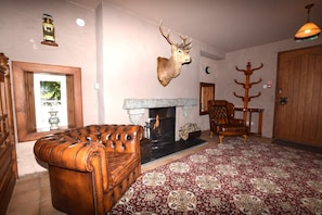 A living room with a fireplace, a leather sofa, a patterned rug, and a deer head mounted on the wall. - 10 Bed in Alness (oc-ca233) (Alness)