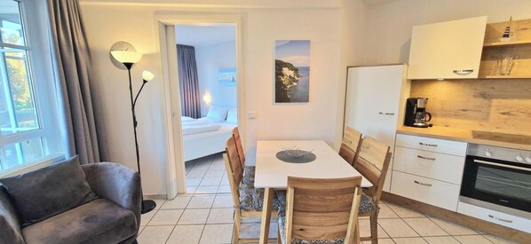A compact hotel room with a dining table, chairs, a sofa, a kitchenette, and a bed in the adjacent room. - Strandnaher Urlaub auf Rugen (Sellin)