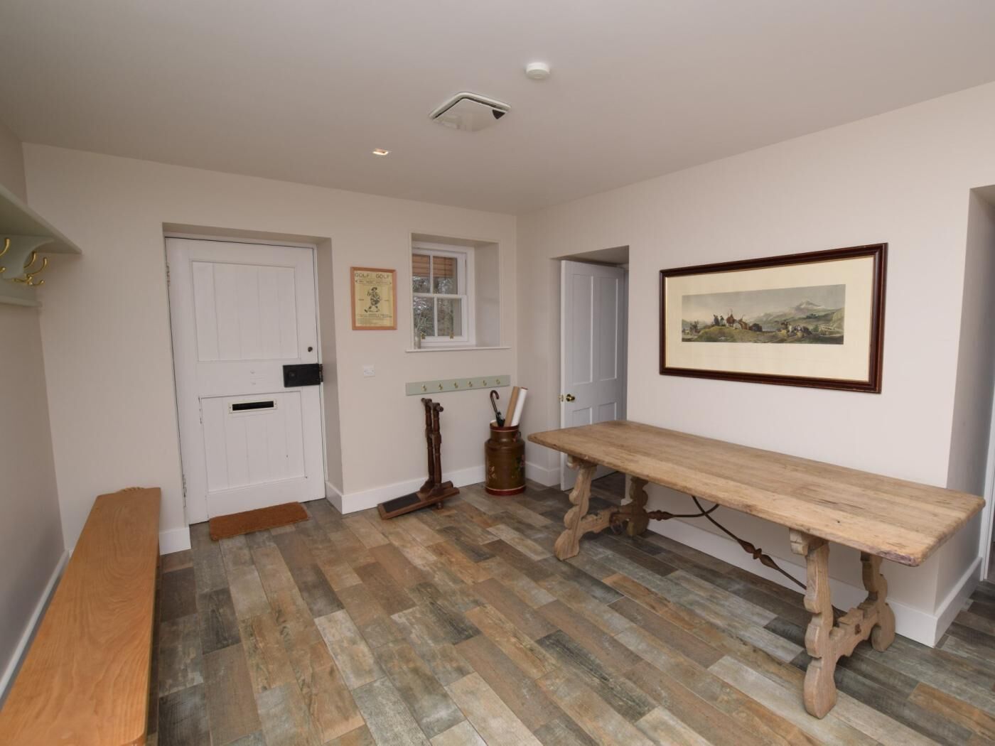A room with a wooden bench, a table, a framed picture, a door, and a window.