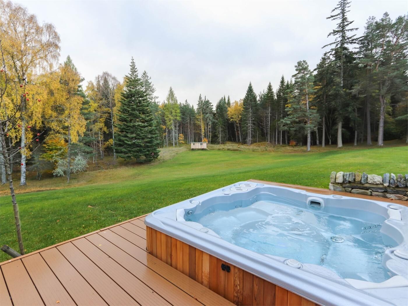 A hot tub on a wooden deck with a view of a grassy area and trees.