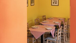 A dining area with tables set for four, wooden chairs, and framed artwork on the wall.
