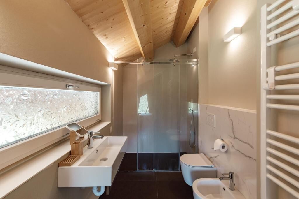 A modern bathroom with a glass shower enclosure, a white sink, and a marble-tiled wall.