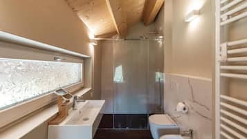 A modern bathroom with a glass shower enclosure, a white sink, and a marble-tiled wall.