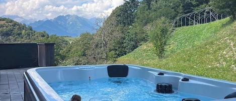A hot tub with a mountain view, two empty wine glasses, and a bottle of champagne on a wooden deck.