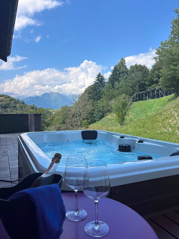 Uma banheira de hidromassagem com vista para as montanhas, dois copos de vinho vazios e uma garrafa de champanhe em um deck de madeira.