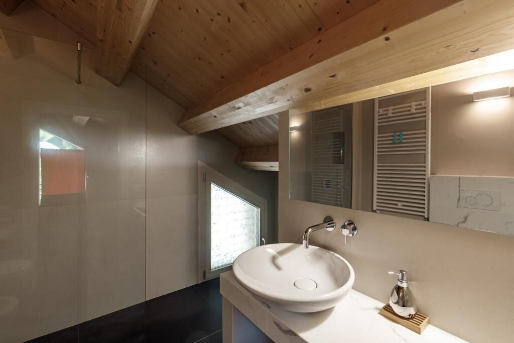 A modern bathroom with a large white sink, a mirror, and wooden ceiling beams.