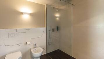 Un baño moderno con inodoro, bidé y ducha con mampara de vidrio.