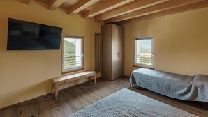 A room with wooden beams, a bench, a bed, a wardrobe, and a TV.
