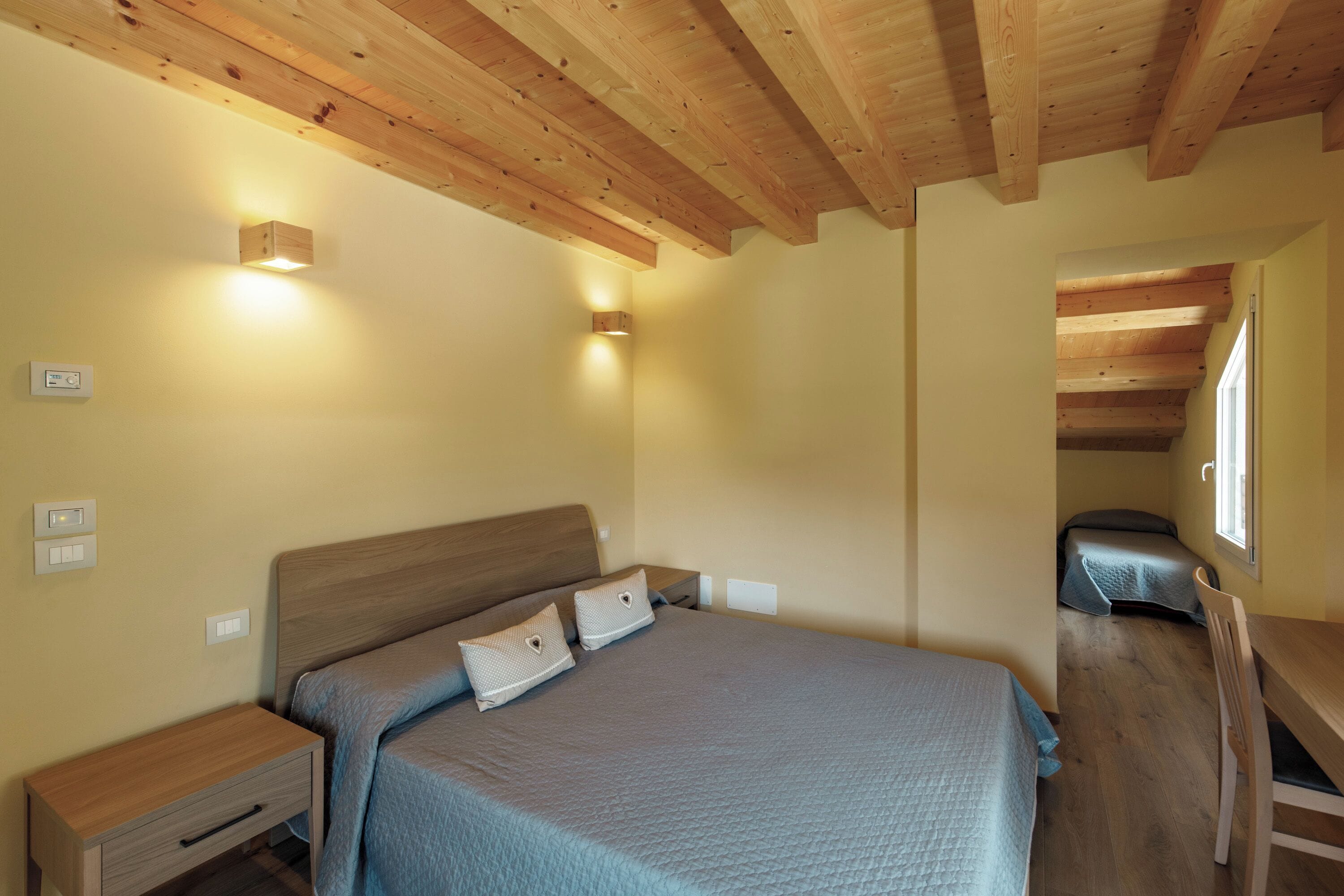 Une chambre avec un plafond en bois, un lit avec une tête de lit, des tables de chevet et un bureau.