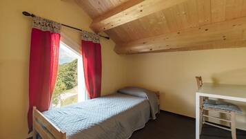 Une petite chambre avec un lit simple, un plafond en bois, une fenêtre avec des rideaux rouges et une petite table avec une chaise.