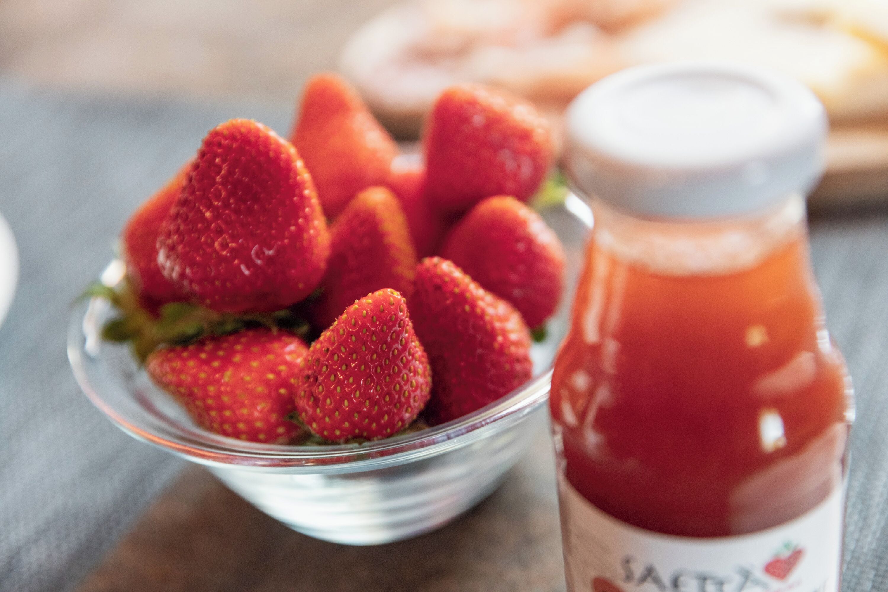 Un bol de fraises à côté d’un pot de confiture de fraises.