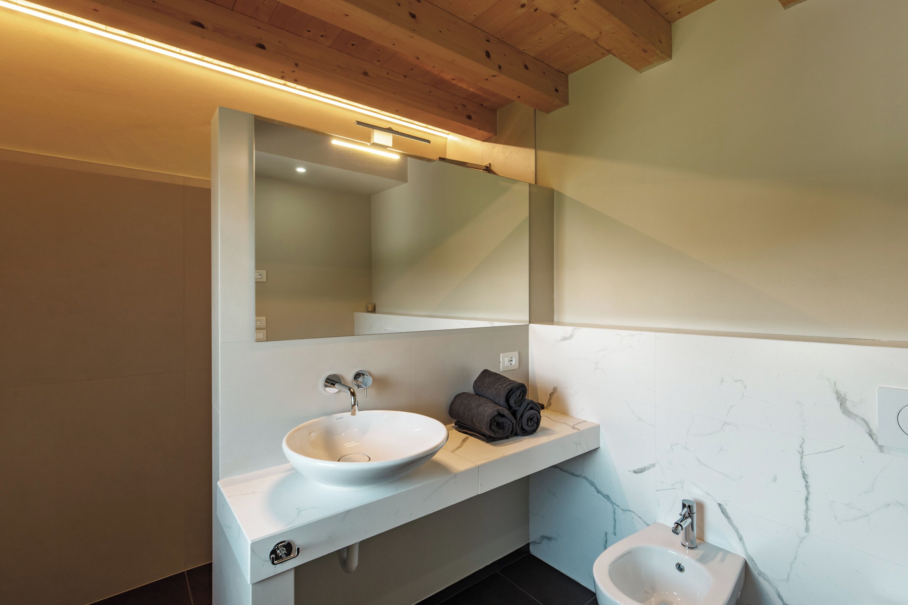 A modern bathroom with a white sink, a mirror, and a small pedestal sink.
