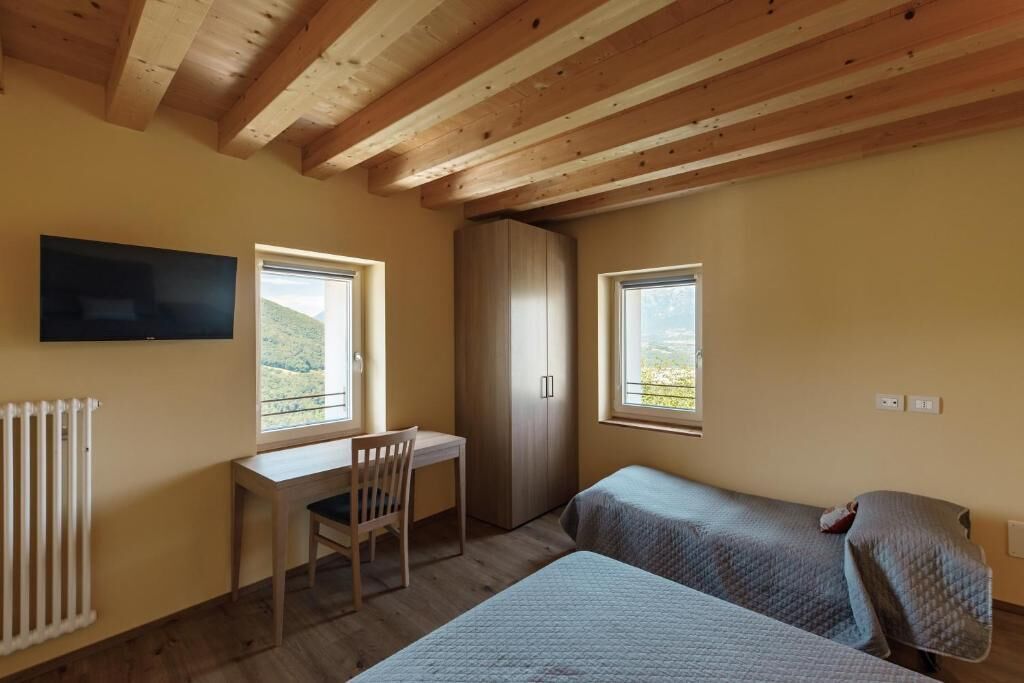A bedroom with two beds, a desk, a chair, a wardrobe, and a TV on the wall.