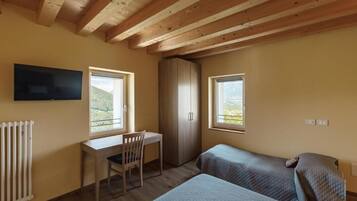 A bedroom with two beds, a desk, a chair, a wardrobe, and a TV on the wall.