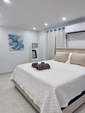 Ein ordentlich bezogenes Bett mit einer weißen Decke und zwei gerollten Handtüchern, ein großer Spiegel an der Wand und eine Klimaanlage über dem Bett.