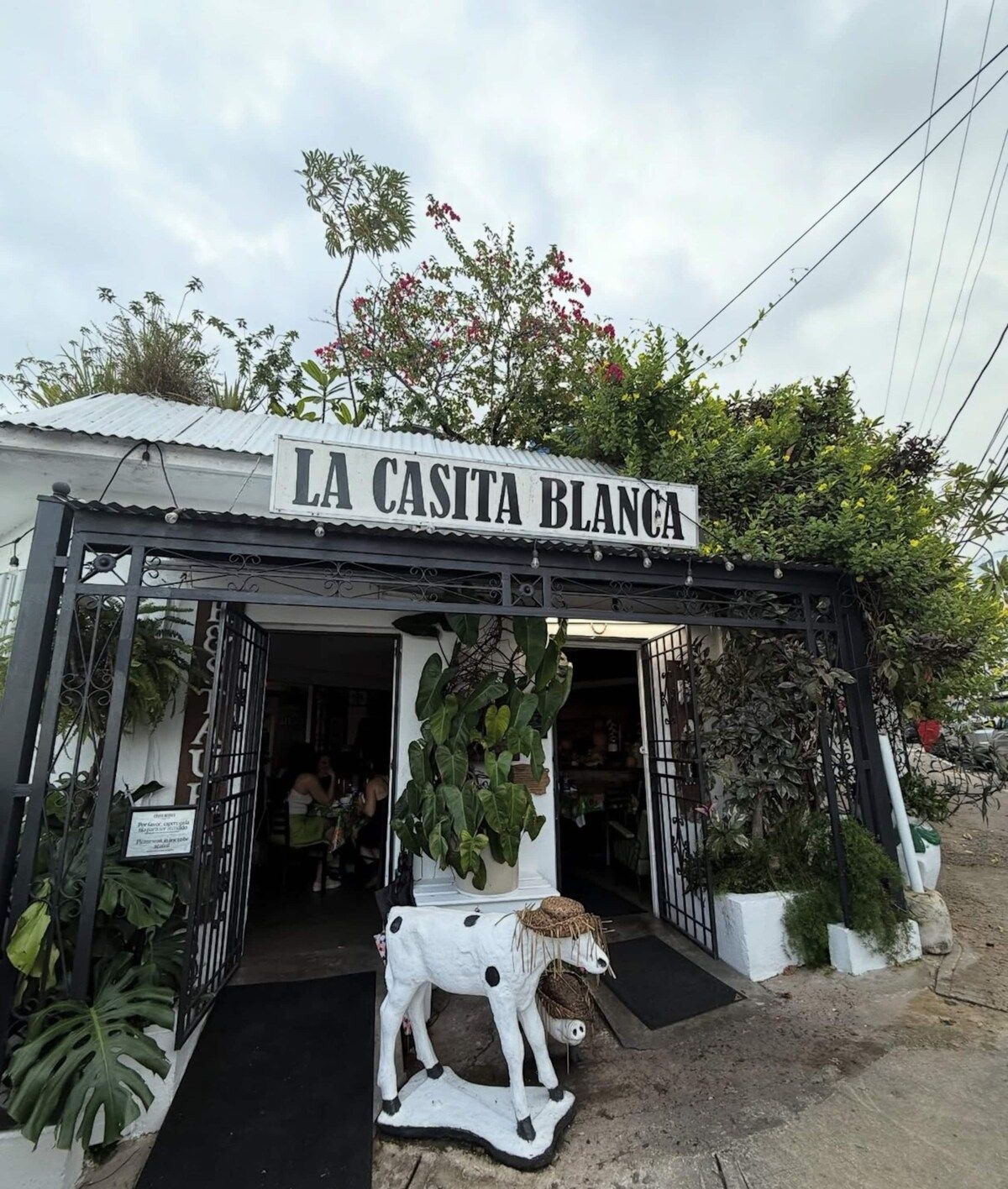 A storefront with a sign reading 'LA CASITA BLANCA' and a cow statue in front.
