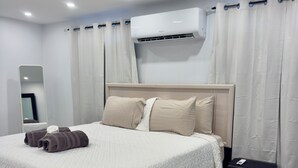 Een moderne slaapkamer met een bed, nachtkastje, spiegel en een airconditioning.