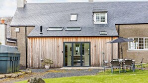 Ein Haus mit geneigtem Dach, einer Holztür und einer Terrasse mit Gartenmöbeln.