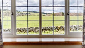 Ein Fenster mit Blick auf ein grünes Feld und eine Steinmauer.