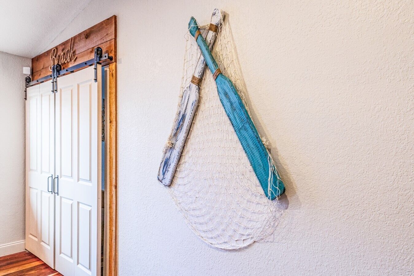Une pièce avec une porte en bois, un mur blanc à texture et un objet rayé de bleu et de blanc accroché au mur.