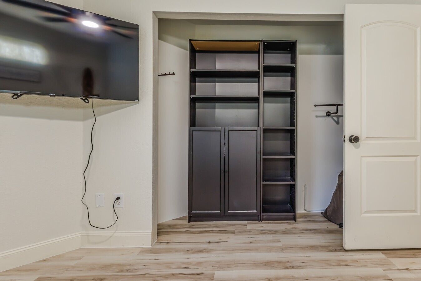 Une pièce avec un téléviseur fixé au mur, une armoire avec plusieurs étagères et une porte.