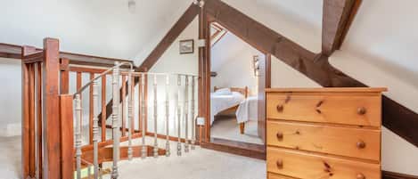 A room with a wooden staircase, a wooden dresser, and a bed in the background.