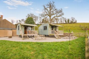 Two small, single-story cabins with porches, a gravel area in front, and a grassy field in the background.