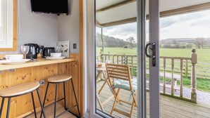 A kitchen with a TV, wooden bar stools, and a view of a grassy field through a glass door.