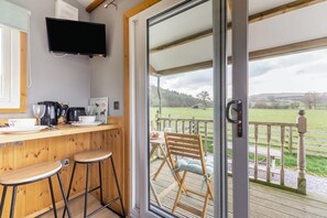A kitchen with a TV, wooden bar stools, and a view of a grassy field through a glass door.