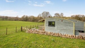 Een klein, laag gebouw met een gebogen dak, een raam en een stenen muur in een grasveld.