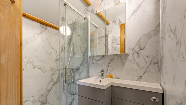 A modern bathroom with a glass shower enclosure, marble walls, and a vanity with a sink and mirror.