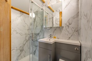 A modern bathroom with a glass shower enclosure, marble walls, and a vanity with a sink and mirror. - 1 Bed in Smardale (oc-e37511) (Smardale)