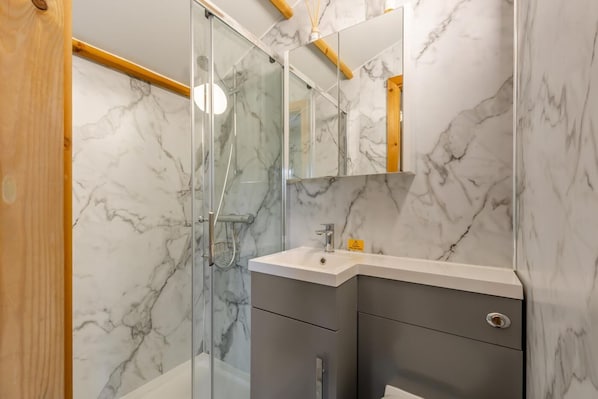 A modern bathroom with a glass shower enclosure, marble walls, and a vanity with a sink and mirror.
