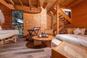 A wooden cabin with a bed, a dining table, and a staircase.