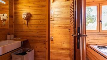 A wooden cabin interior with a wooden wall, a white sink, a towel rack, and a window.