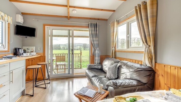 Een gezellige kamer met een leren bank, een houten tafel, een keukenhoek en een schuifdeur naar een balkon.