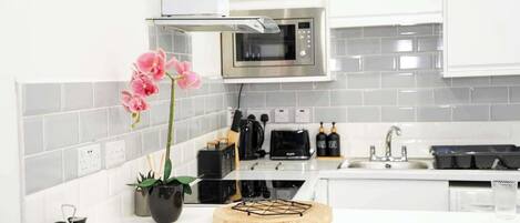 A modern kitchen with white cabinets, a stainless steel microwave, a black toaster, and a sink.