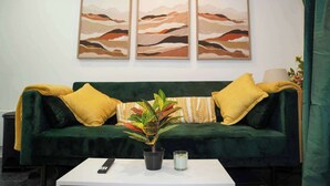 A green sofa with yellow cushions, a potted plant, a remote control, and three abstract paintings on the wall.