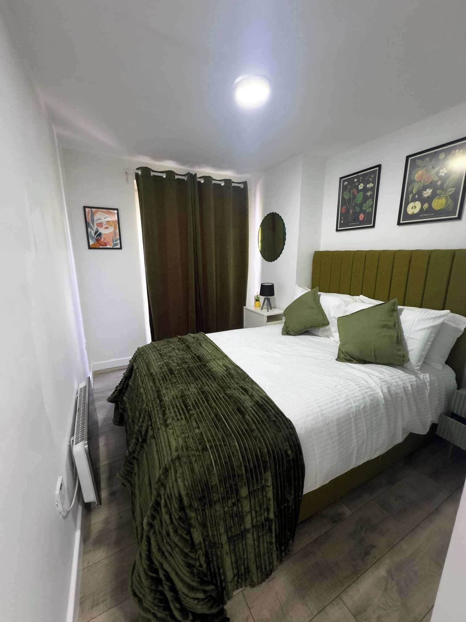 Una camera da letto con un letto, un comodino, una lampada, una finestra con tende e uno specchio fissato al muro.