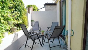 An outdoor seating area with four chairs and a table, a potted plant, and a hose connected to a wall-mounted device.