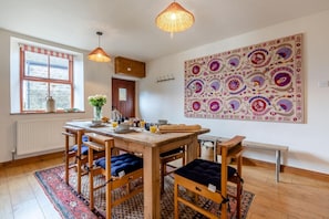 A dining area with a wooden table, chairs, and a large decorative wall hanging. - 3 Bed in Longnor (oc-r34925) (Longnor)
