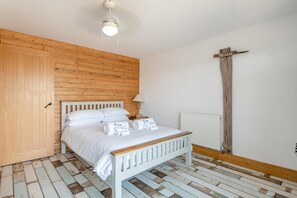 Ein Schlafzimmer mit einem hölzernen Kopfteil, einem Bett mit weißen Leinen, einem Nachttisch, einer Lampe und einem Holzkreuz an der Wand.