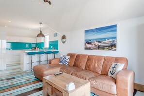 Ein modernes Wohnzimmer mit Ledersofa, Couchtisch aus Holz und einer Küchenzeile mit Barhocker.