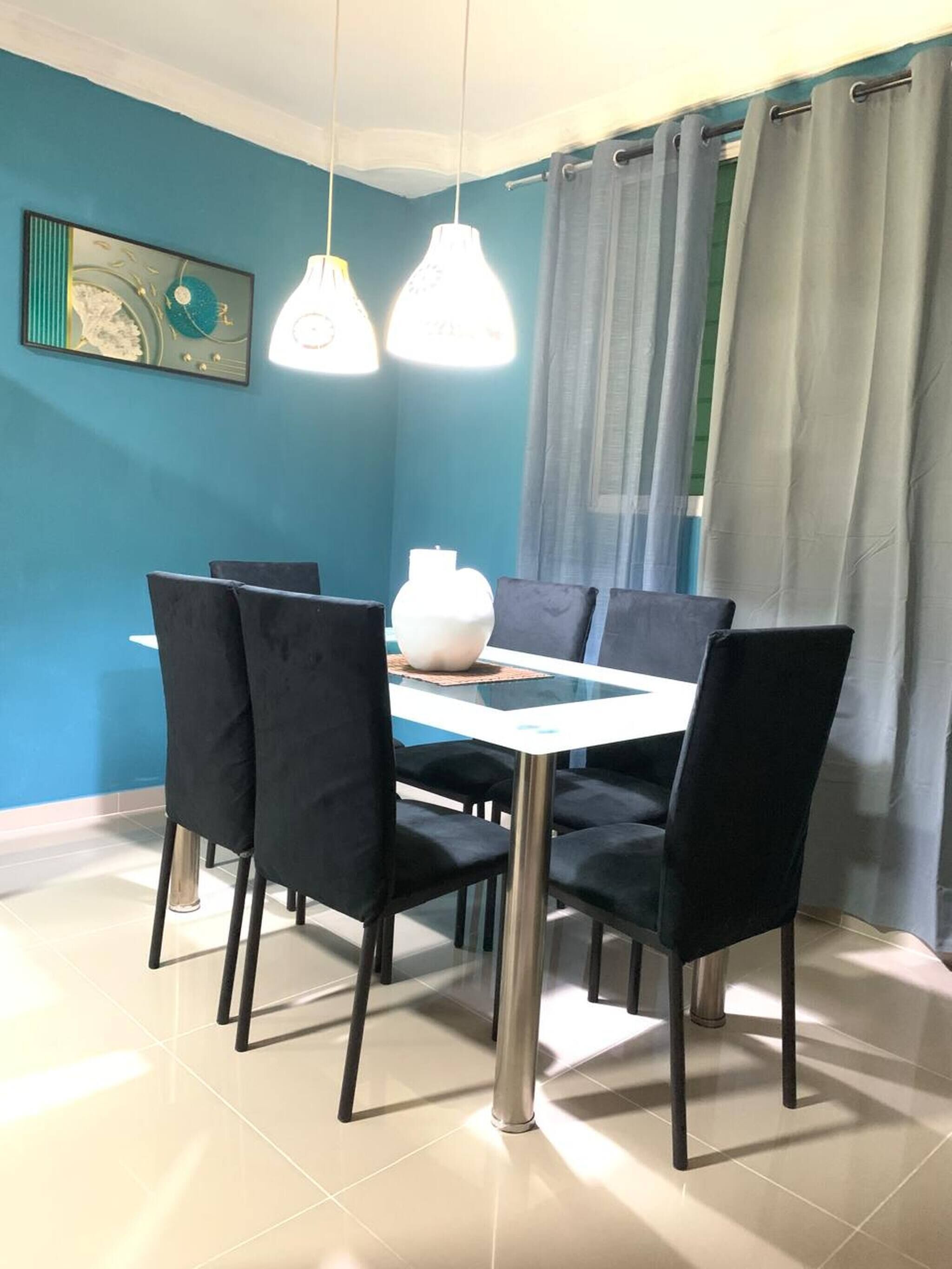 Un espace repas comprenant une table, des chaises, des luminaires suspendus et un rideau.