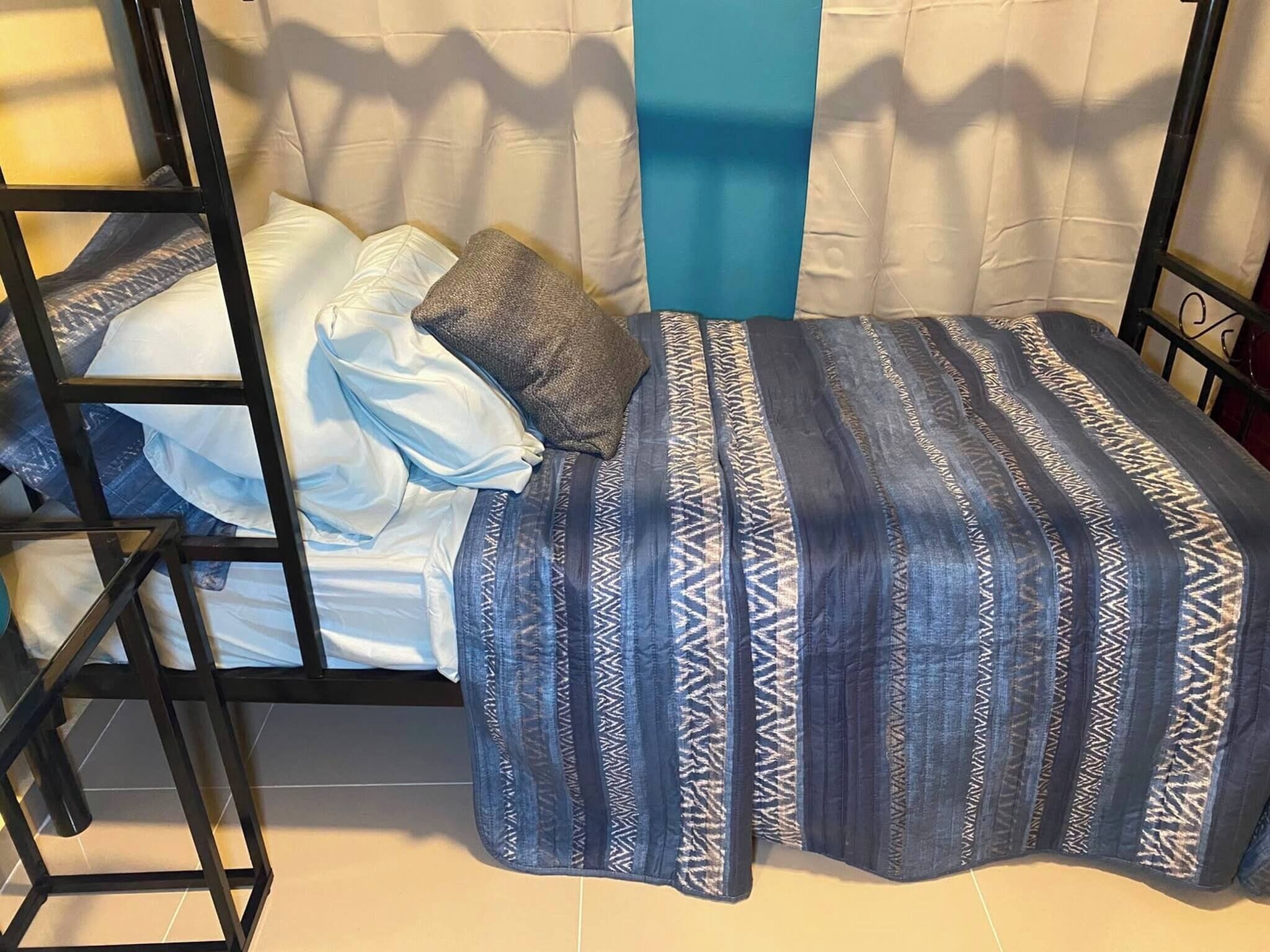 Una cama litera con colcha estampada, almohadas y una pared azul decorativa.