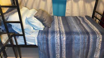Una cama litera con colcha estampada, almohadas y una pared azul decorativa.