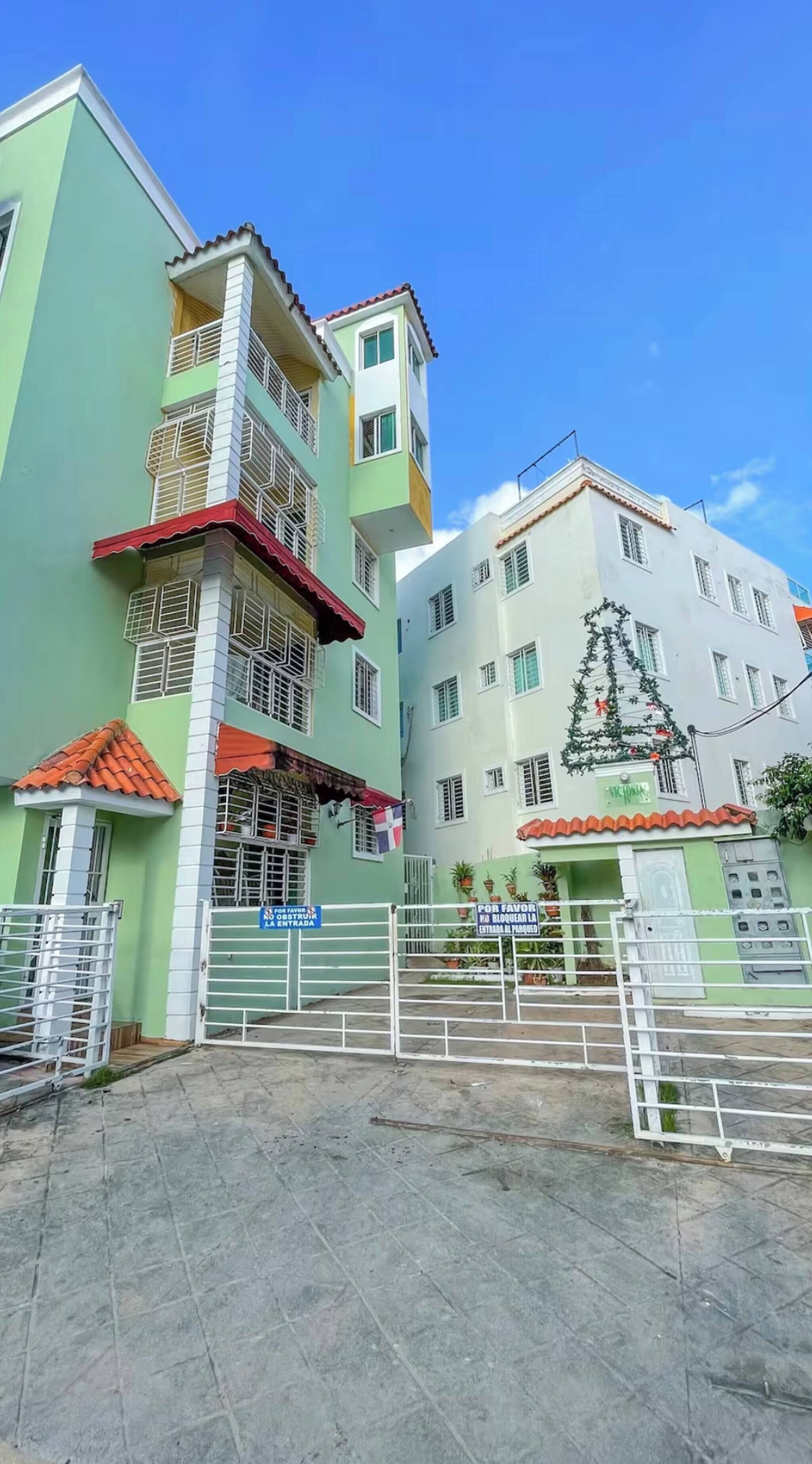 A multi-story building with a green facade, a red roof, and a white gate.